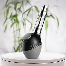 A Lookah Egg 510 thread battery placed on a white surface with a blurred green plant background.